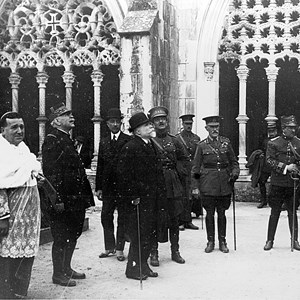 O Presidente da República António José de Almeida, em primeiro plano, usando chapéu de coco, visita o túmulo do Soldado Desconhecido da Grande Guerra, no Mosteiro de Santa Maria da Vitória. Acompanham-no, entre outros: o bispo de Leiria, à esquerda; o marechal francês Joseph Joffre, o segundo a contar da esquerda; o general inglês Smith-Dorrien, o quarto a contar da direita.