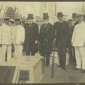 O presidente do Governo António José de Almeida, ao centro, de cartola, a bordo de um navio da Armada portuguesa, acompanhado pelo Presidente da República Bernardino Machado, ao centro, de bengala e luvas.