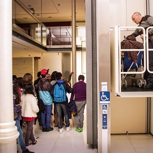 Visitante utilizando o ascensor de acesso ao 1.º Piso do Museu; paralelamente, decorre uma visita guiada a grupo de alunos do ensino básico do distrito de Bragança.