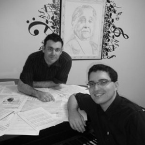 Alexandre Dias e Wandrei Braga, pianistas que têm estudado a obra de Chiquinha Gonzaga e que em 2011 criaram o projeto «Acervo Digital Chiquinha Braga». Atrás, o retrato da artista.