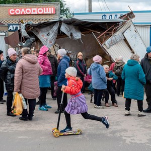 Lera (10 anos) anda de trotineta junto a uma fila para ajuda humanitária, na cidade recentemente libertada de Izium.